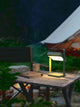 LED Akkuleuchte Saulio Solar IP44 auf einem Tisch neben einer Campingliege bei Nacht.