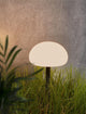 LED Akkuleuchte Sponge Spike IP65 in elegantem, pilzförmigem Design im Gras vor einer Betonwand.