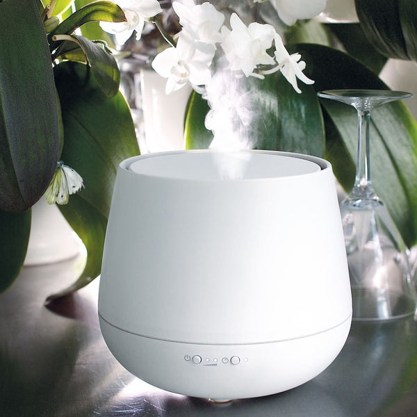 LED Aroma Diffuser Julia rumduftspreder i et elegant design med æterisk damp mellem planter.