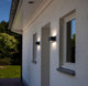LED Außenwandleuchte Gemini IP54 in Anthrazit an einer weißen Wand neben Fenstern montiert.