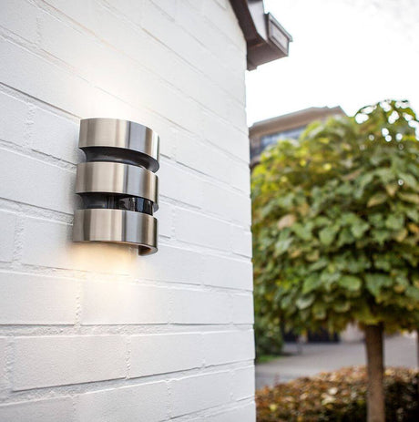 LED Außenleuchte Maya IP44 Edelstahl mit Bewegungsmelder an einer Wand installiert, strahlt modernes Licht aus.