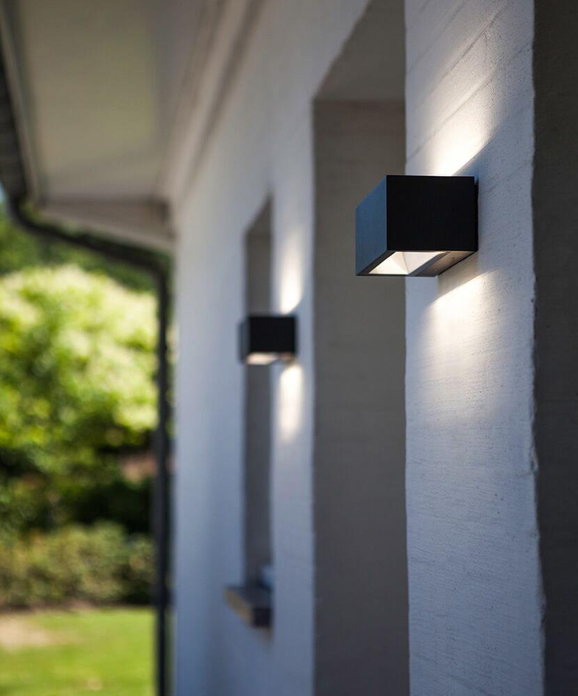 LED Außenwandlampe Gemini IP54 Anthrazit an einer weißen Wand montiert, strahlende Up-&-Down-Lichteffekte.