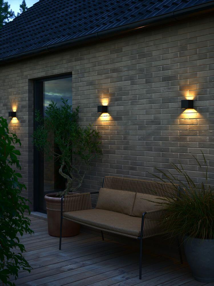 LED Außenwandlampe Milda kubi IP44 an einer Wand mit Sofa und Pflanzen, für minimalistisches Design und Lichteffekte.