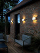 LED Außenwandlampe Piola IP44 beleuchtet eine Hausfassade bei Nacht, moderne Wandleuchte mit geschwungenem Design.