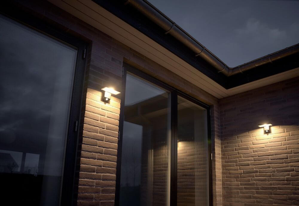 LED Außenwandlampe Rica Square Solar IP44 an einer Backsteinwand montiert, beleuchtet den Eingang.