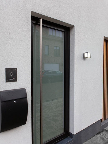 LED Außenwandlampe Telin IP54 Anthrazit neben einer modernen Glastür an einem Haus.