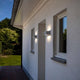 LED Außenwandleuchte Gemini IP54 Weiß an einer weißen Wand montiert, beleuchtet den Eingangsbereich.