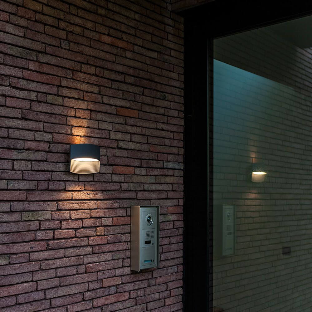 LED Außenwandleuchte Lotus IP54 Anthrazit an einer Backsteinwand montiert, warmweißes Licht ausstrahlend.