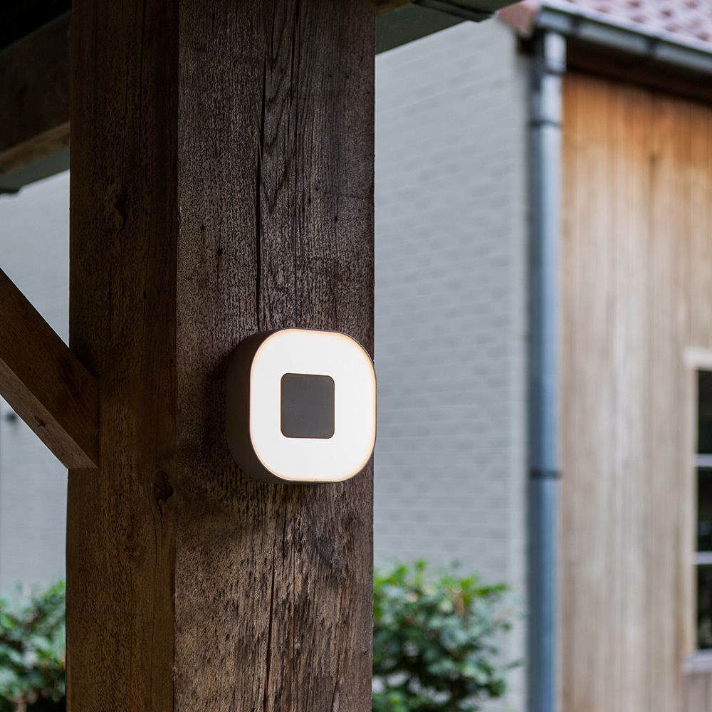 LED Außenwandleuchte Ublo 33x23cm in Grau an einer Holzstütze im Außenbereich.