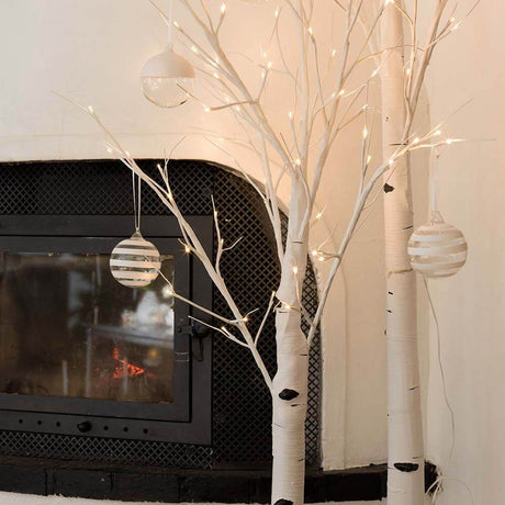 LED Birke groß weiß 120 Warmweiße Dioden mit dekorativen Kugeln und Kamin im Hintergrund.