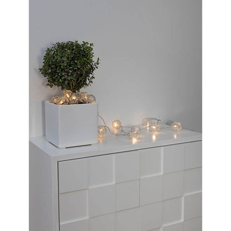 LED decorative light chain aluminum wire balls small 16 warm white diodes battery-operated on a sideboard with plant.
