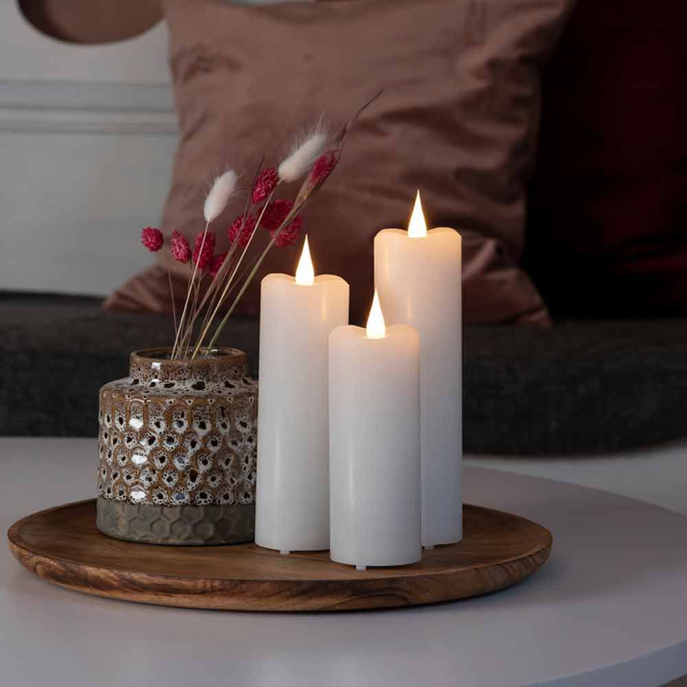 LED Echtwachskerzen in Weiß mit Timer, dekorativ auf einem Tisch mit einer Vase und Trockenblumen.