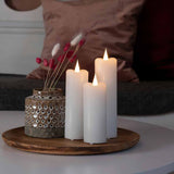 LED Echtwachskerzen in Weiß mit Timer, dekorativ auf einem Tisch mit einer Vase und Trockenblumen.