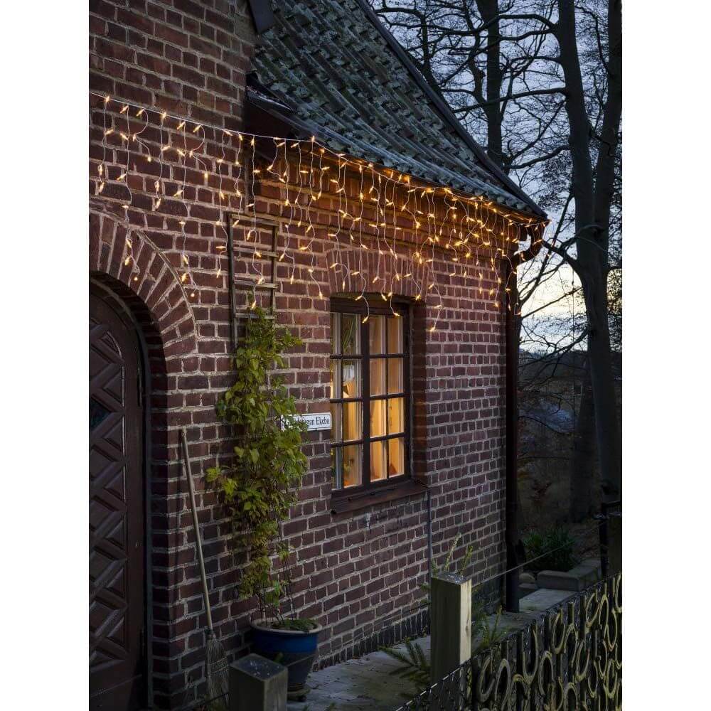 LED Eisregen Lichtervorhang 200 bernsteinfarbene Dioden 31V IP44 beleuchtet eine brick house at dusk.