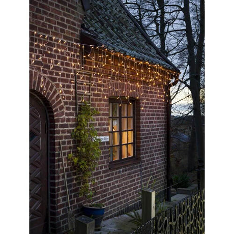 LED Eisregen Lichtervorhang 200 bernsteinfarbene Dioden 31V IP44 beleuchtet eine brick house at dusk.