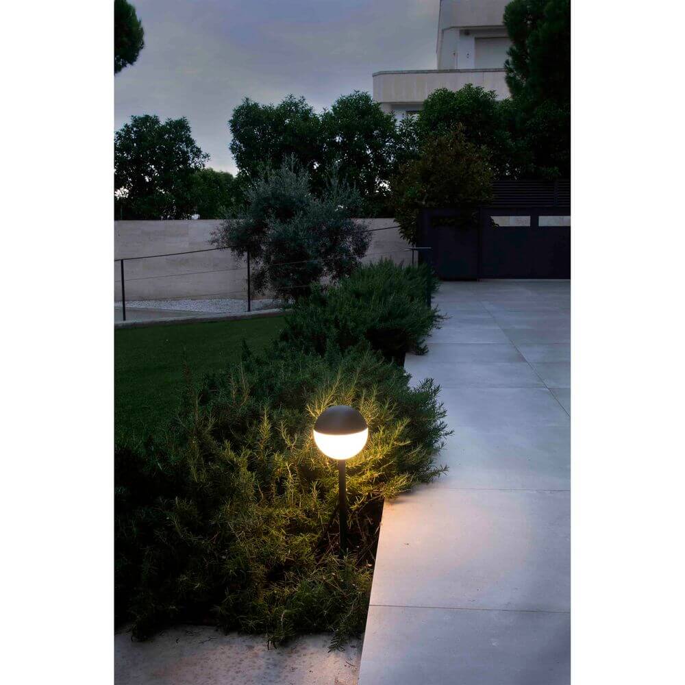 LED Wegelampe mit Erdspieß PICCOLA 2700K IP65 Schwarz leuchtet im Garten bei Dämmerung.