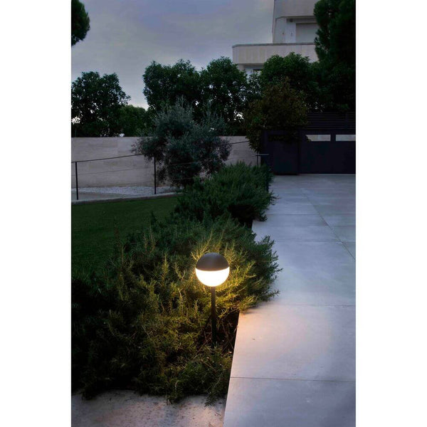 LED Wegelampe mit Erdspieß PICCOLA 2700K IP65 Schwarz leuchtet im Garten bei Dämmerung.