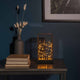 LED Glaslaterne mit schwarzem Holzfundament und 6h Timer Schwarz auf einem Tisch mit Büchern und Dekoration.