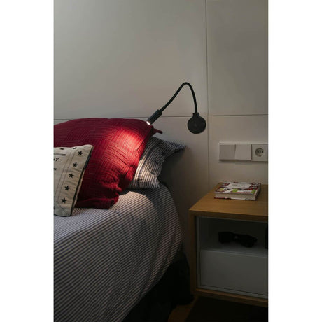 LED PIXIE 3W 2700K Sort læselys over en seng med røde puder og natbord.
