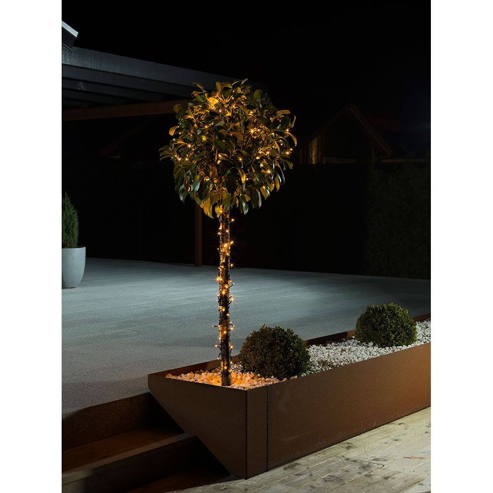LED Lichterkette mit Glimmereffekt 160 bernsteinfarbene Dioden (80 glimmend) IP44 dekoriert einen Baum im Garten.
