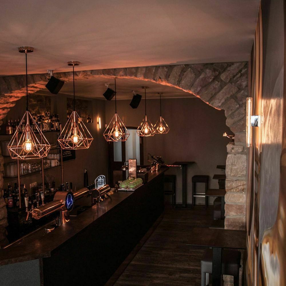 Stylische Bar mit geometrischen Hängeleuchten und dunklem Bartresen, gemütlicher Atmosphäre.