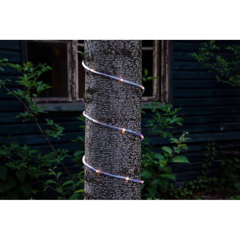 LED Mini Lichterschlauch 5m mit Lichtsensor Timer 65 Warmweiße Dioden batteriebetrieben IP44 um einen Baum gewickelt bei Nacht.
