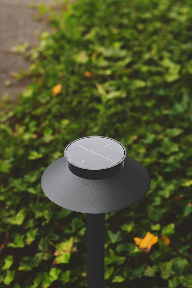 LED Pollerleuchte Justina Solar IP44 auf grünem Hintergrund mit Blättern.