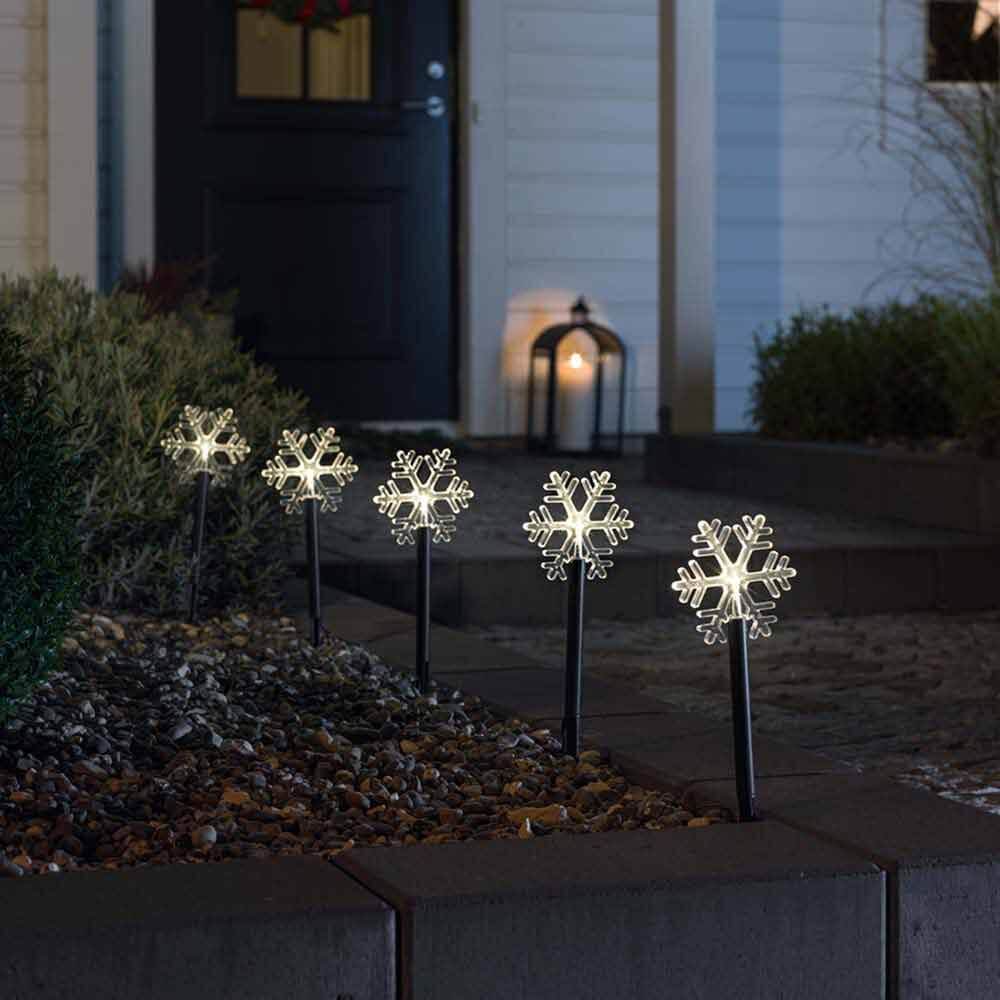 LED Spießleuchte mit 5 Schneeflocken Klar in einem dekorativen Gartenbeet bei Nacht.