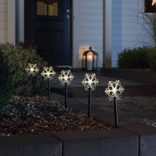 LED Spießleuchte mit 5 Schneeflocken Klar in einem dekorativen Gartenbeet bei Nacht.