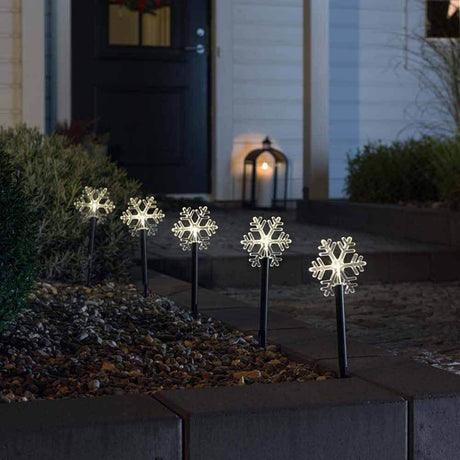 LED Spike light with 5 clear snowflakes in a decorative garden bed at night.