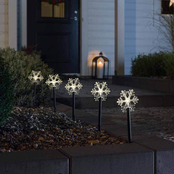 LED Spießleuchte mit 5 Schneeflocken Klar in einem dekorativen Gartenbeet bei Nacht.