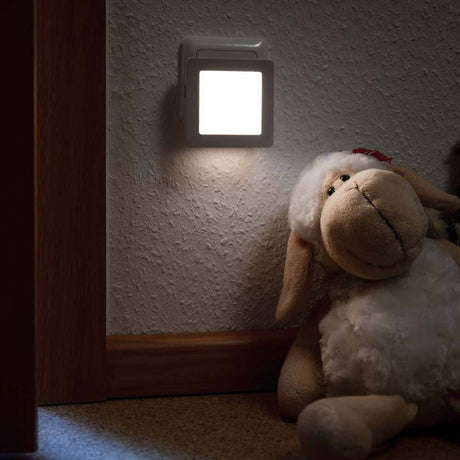 LED Steckerlicht Esby mit Sensor 3000K Weiß leuchtet sanft neben einem flauschigen Schaf in einem dunklen Raum.