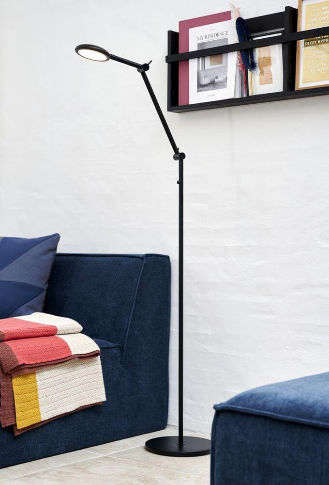 LED Stehlampe Bend Single in modernem Wohnzimmer mit blauen Sofas und bunten Decken.