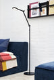 LED Stehlampe Bend Single in modernem Wohnzimmer mit blauen Sofas und bunten Decken.