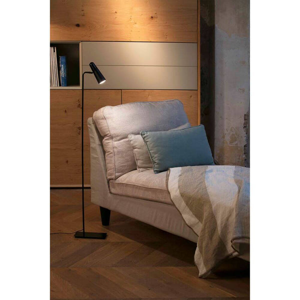 Moderne LED Stehlampe LAO Schwarz neben einem gemütlichen Sessel und einer Decke in einem stilvollen Raum.