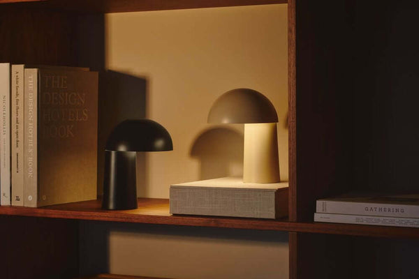 LED Lampe de table Faye Portable sur une étagère avec des livres, diffusant une lumière douce.