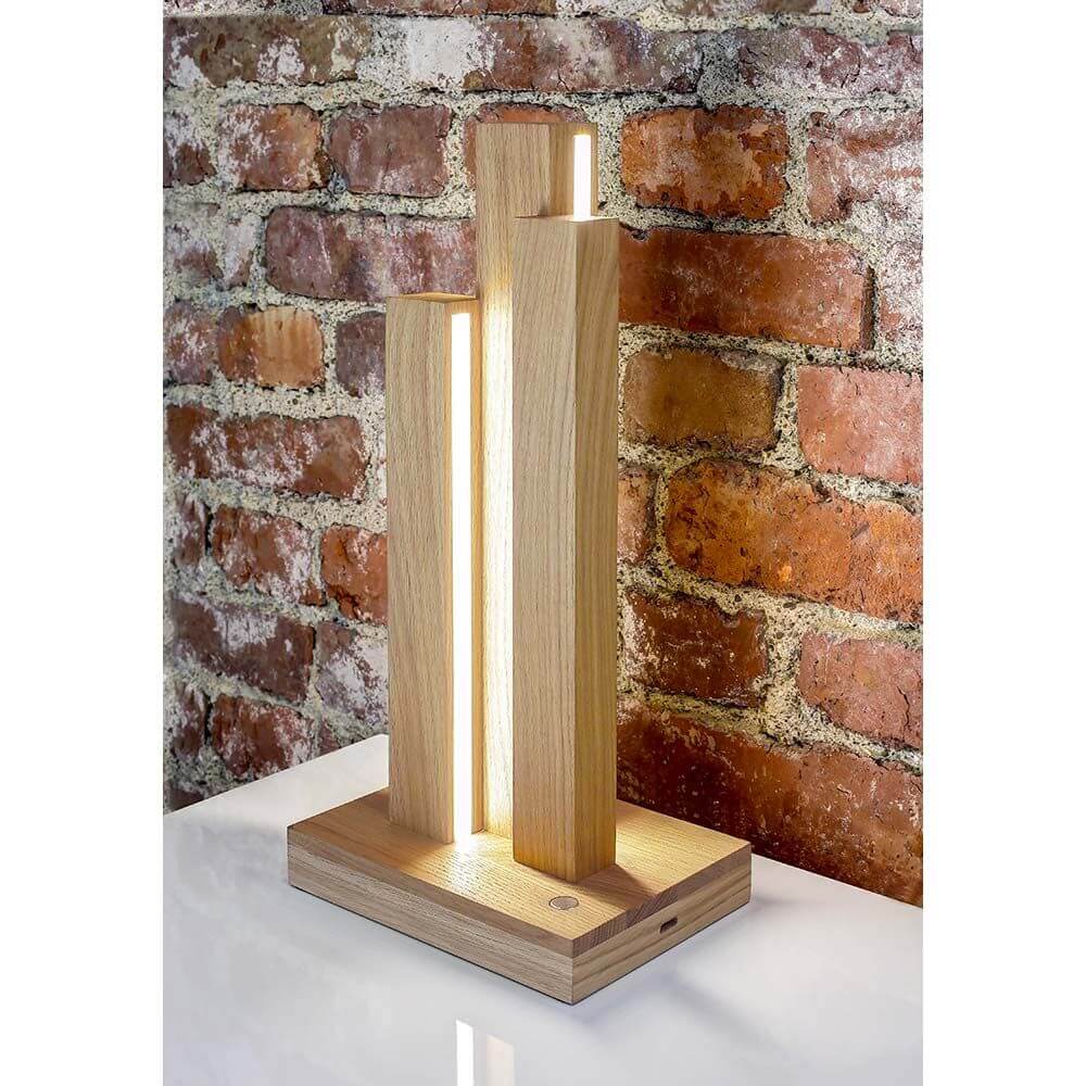 LED Tischleuchte Manhattan Touch-Dimmer 910lm Eiche-Geölt auf einem Tisch vor einer Backsteinmauer.