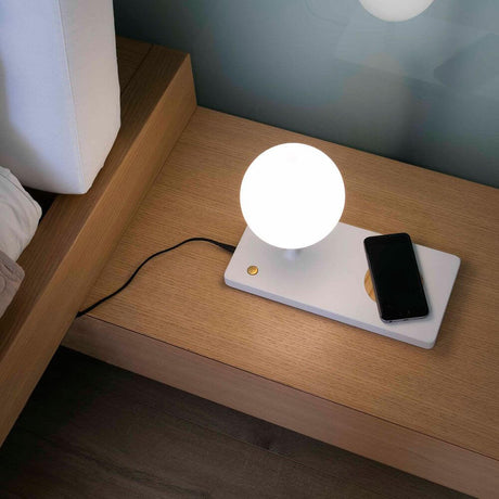 LED Tischleuchte NIKO mit induktiver Handy Ladestation auf einem Nachtisch.