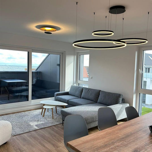 Modernes Wohnzimmer mit schwebenden Lampen, grauem Sofa und großen Fenstern mit Meerblick.