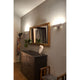 LED Wandlampe CONIK 8W 3000K 800lm Weiß an einer Wand über einem schwarzen Sideboard mit Spiegel und Pflanzen.