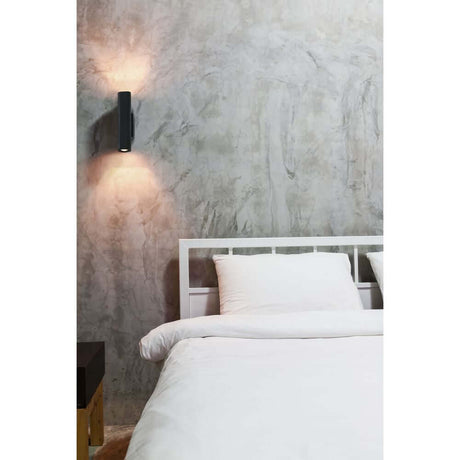 LED Wandlampe LISE 12W 2700K Schwarz an einer Wand über einem Bett, modernes und elegantes Design.