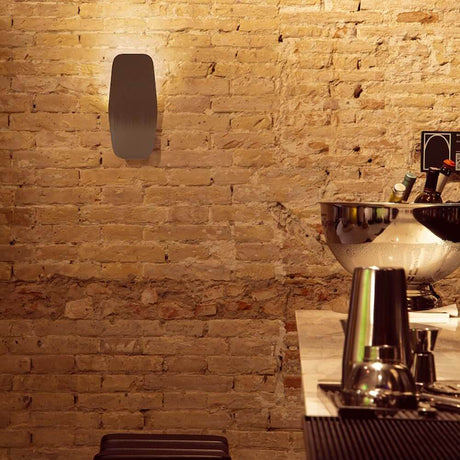 Moderne LED-Wandleuchte ASHIYA aus gebogenem Aluminium an einer Backsteinwand in einer stilvollen Bar.