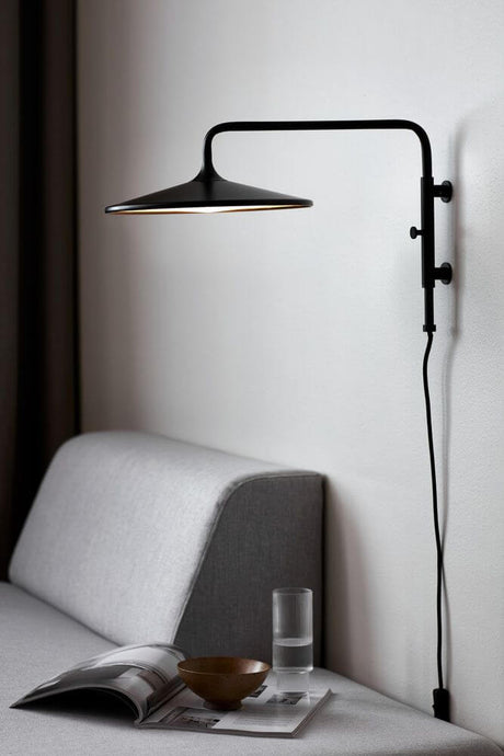 LED Applique murale Balance sur un mur au-dessus d’un canapé gris avec un magazine et un verre d’eau.