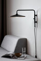 LED Wandleuchte Balance an einer Wand über einer grauen Couch mit einem Magazin und einem Glas Wasser.