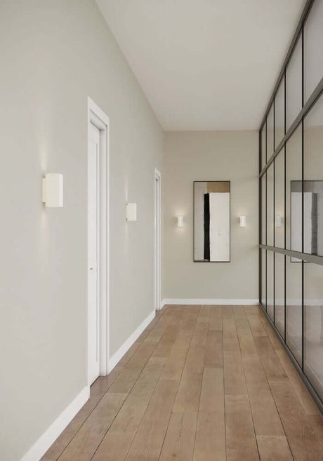 LED Wandleuchte Curtiz beleuchtet einen modernen Flur mit Holzfußboden und großen Fenstern.