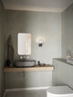 LED Wandleuchte Hester IP44 im modernen Badezimmer mit Holzregal und runder Spiegelfläche.