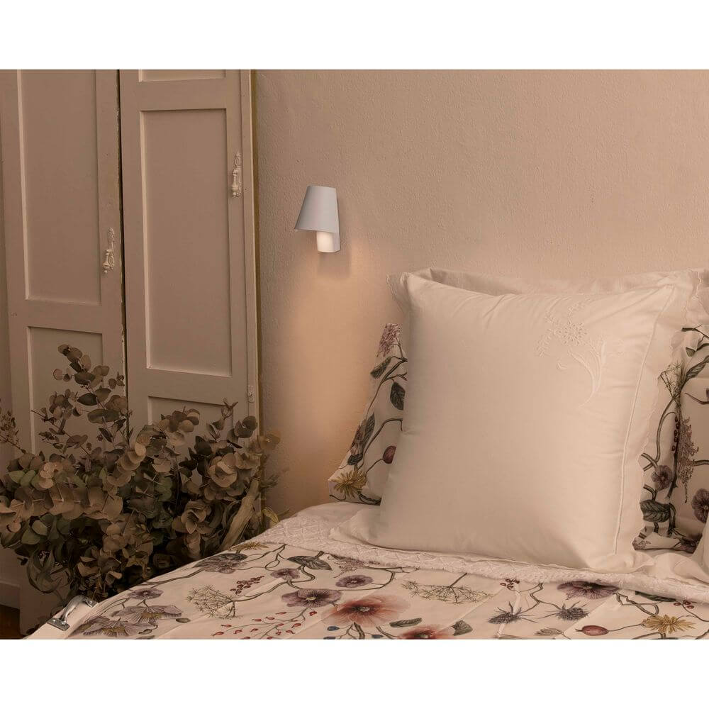 LED Wandleuchte LE PETIT Weiß neben Bett mit Kissen und dekorativen Pflanzen.