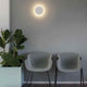 Moderne LED Wandleuchte LUNA 5W 2700K Weiß an der Wand über zwei grauen Stühlen in einem gemütlichen Raum.
