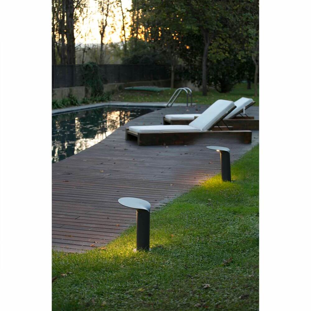 LED Wegeleuchte Lotus 35cm 18W 3000K IP65 Dunkelgrau in Gartenlandschaft mit Pool und Liegen.