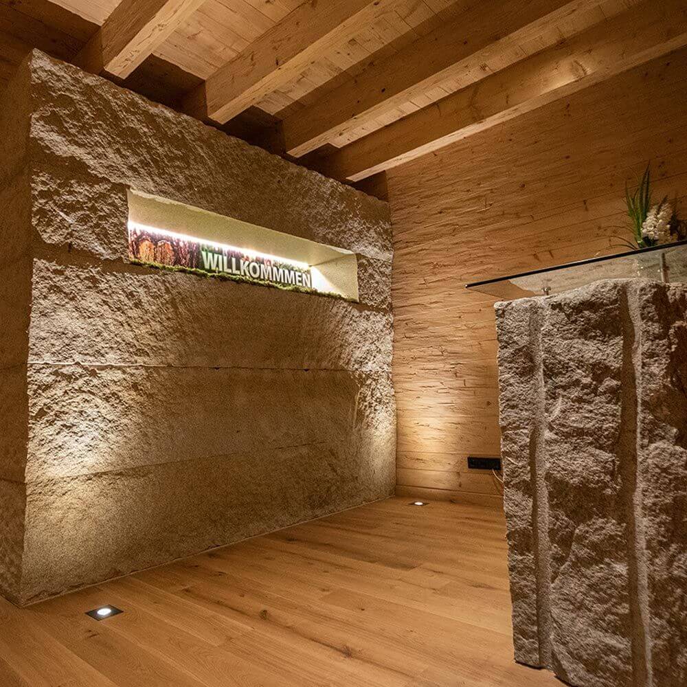 Moderner Raum mit steinerner Wand, Holzdetails und LED-Beleuchtung, Willkommen-Schild in der Nische.